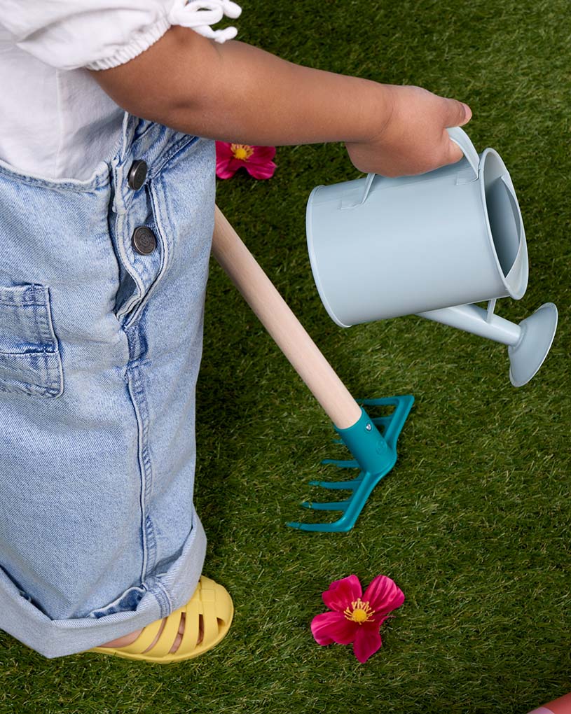 Kind gießt Wasser in blauen Sandkasten draußen.