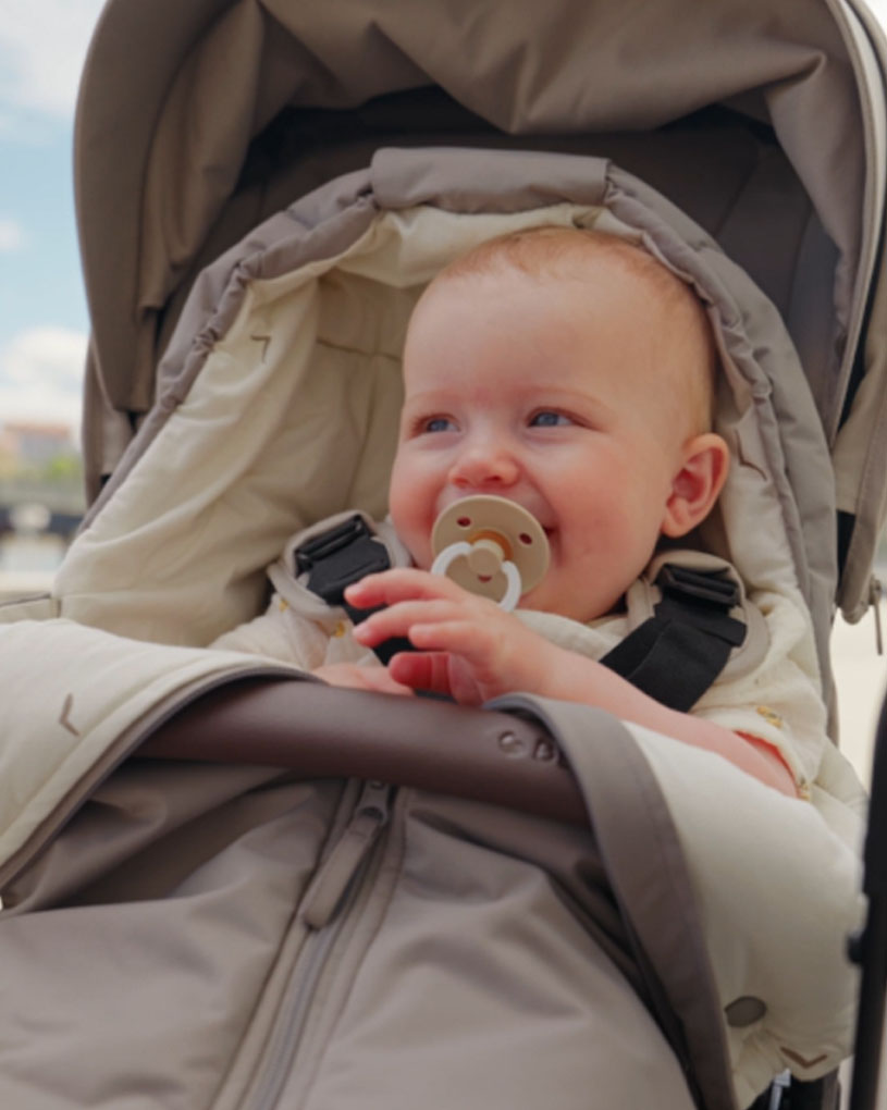 Baby im Kinderwagen mit Schnuller im Mund, vor blauem Himmel.