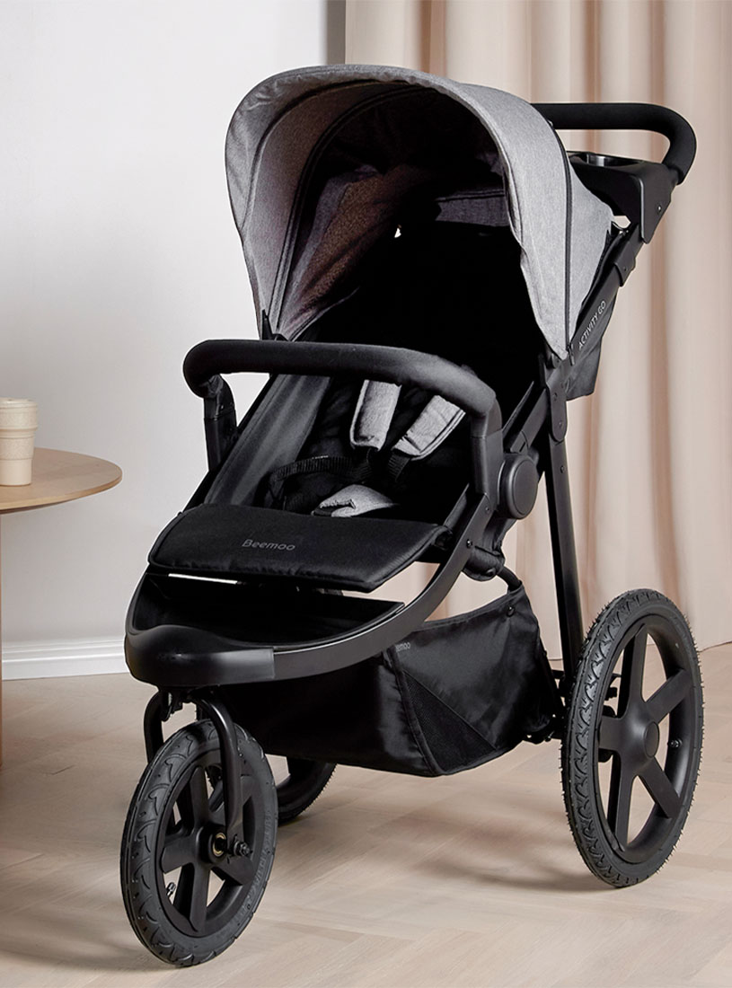 Schwarzer Kinderwagen mit drei Rädern steht drinnen neben einem Tisch.