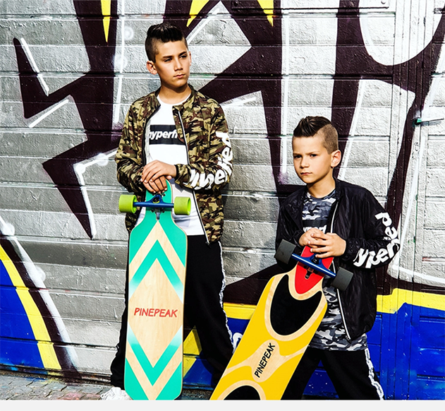 Zwei Jungen posieren mit Longboards vor einer Graffiti-Wand.