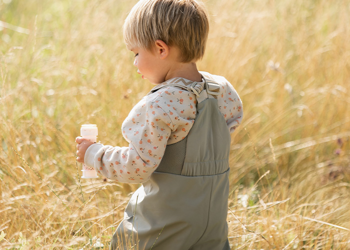 Kind in grauem Overall hält eine Flasche, mit dem Text 'Kenza X Viking'.