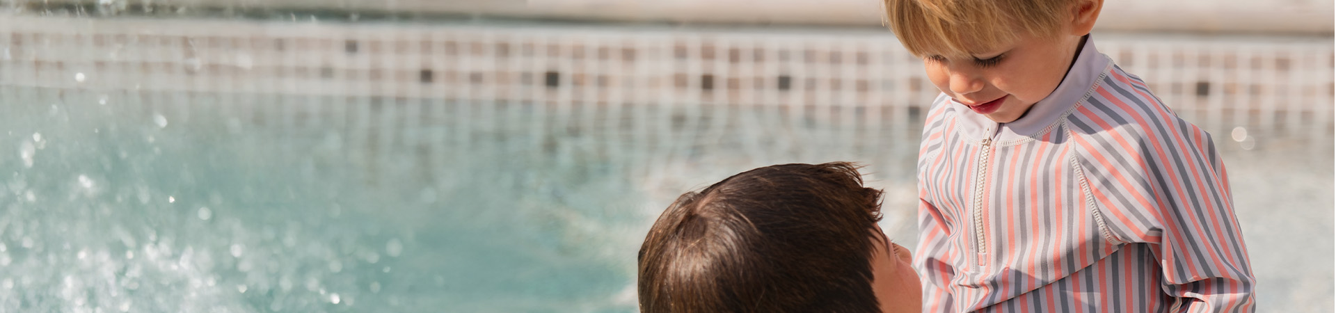 Eine Mutter lächelt ihrem Kind zu, das eine Blume hält, mit dem Text 'Kenza X Viking'.