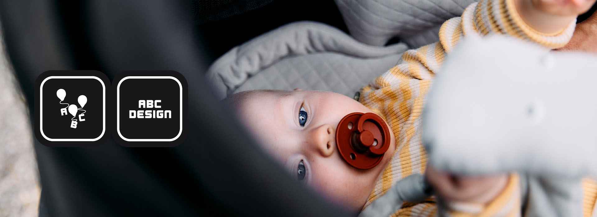 Baby mit Schnuller liegend im Kinderwagen mit Logo 'ABC Design'.
