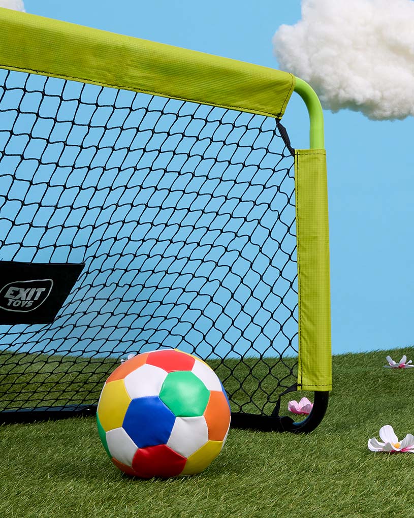 Kind mit Mütze spielt draußen mit Ball.