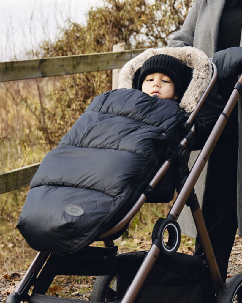 Kind im Kinderwagen mit schwarzem Fußsack, beim Spaziergang.
