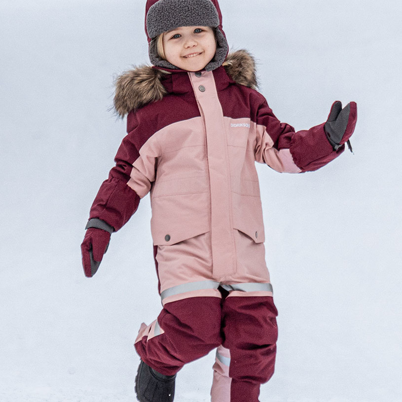 Kind in Winteroverall und Mütze spielt im Schnee.