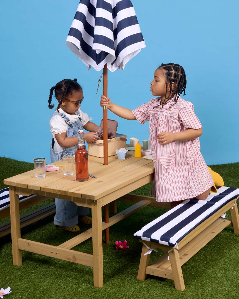 Kind in Sonnenbrille und Leopardenpyjama auf Bank mit Kissen.