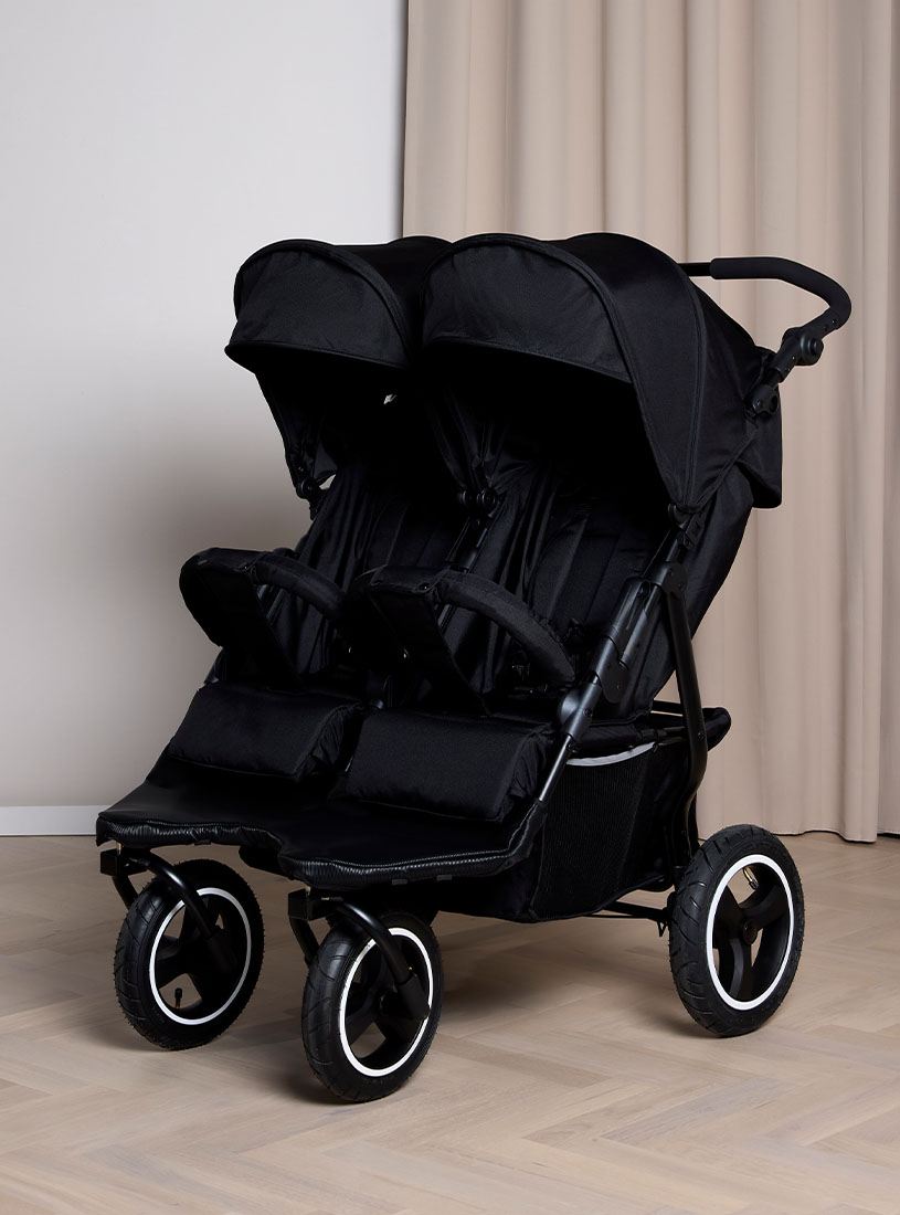 Schwarzer Doppelkinderwagen mit vier Rädern drinnen.