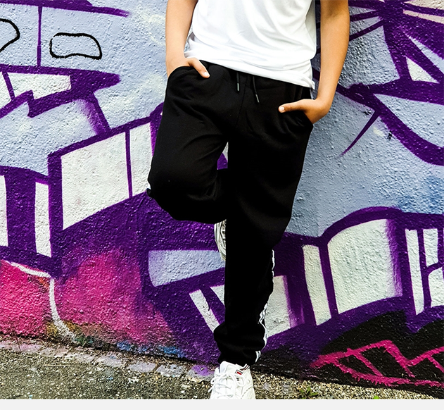 Person an Graffiti-Wand, trägt T-Shirt und Hose.