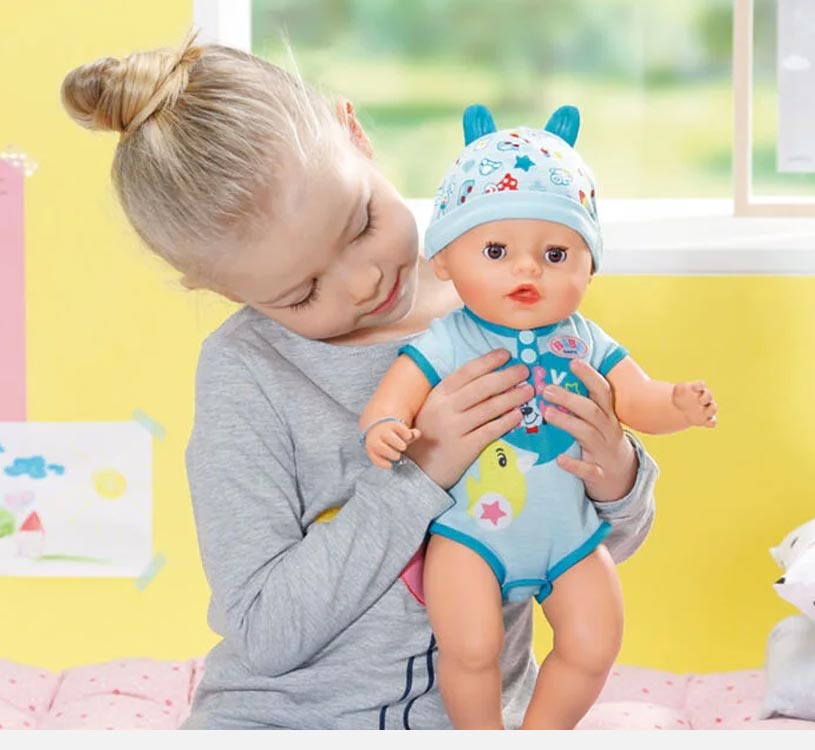 Mädchen hält eine Puppe in blauer Kleidung mit Mütze.