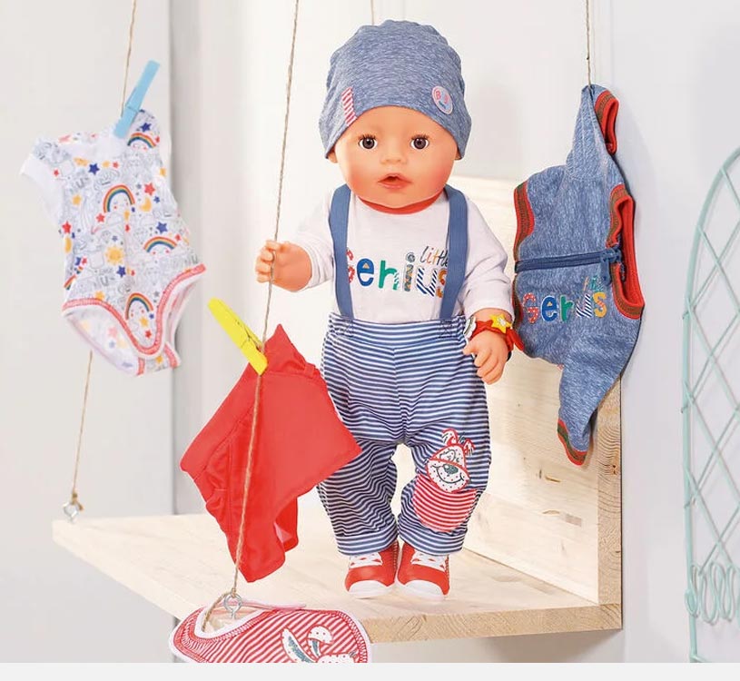 Puppe mit gestreifter Hose und Mütze auf Regal, umgeben von Babykleidung.