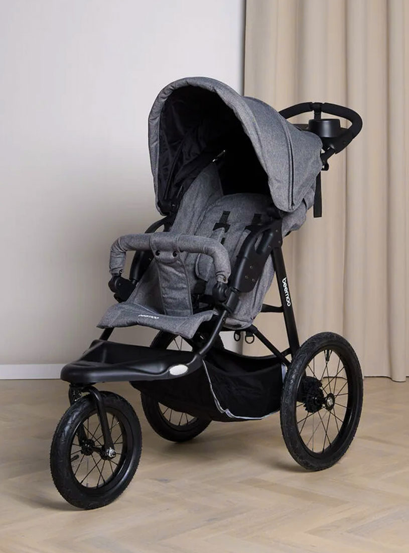 Grauer Jogging-Kinderwagen mit drei Rädern vor beigem Vorhang.
